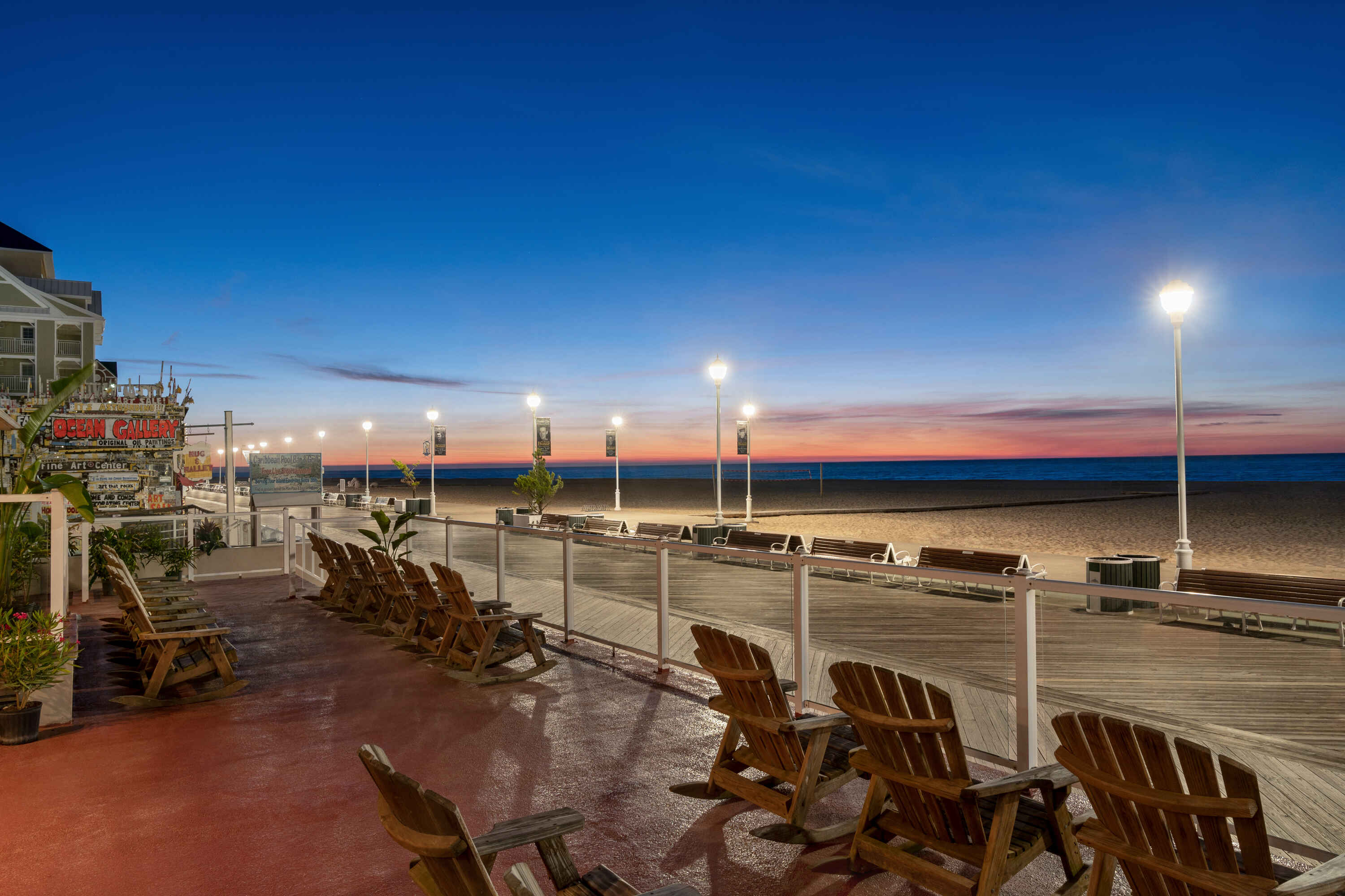 A beachfront pier at sunset with wooden chairs and a railing