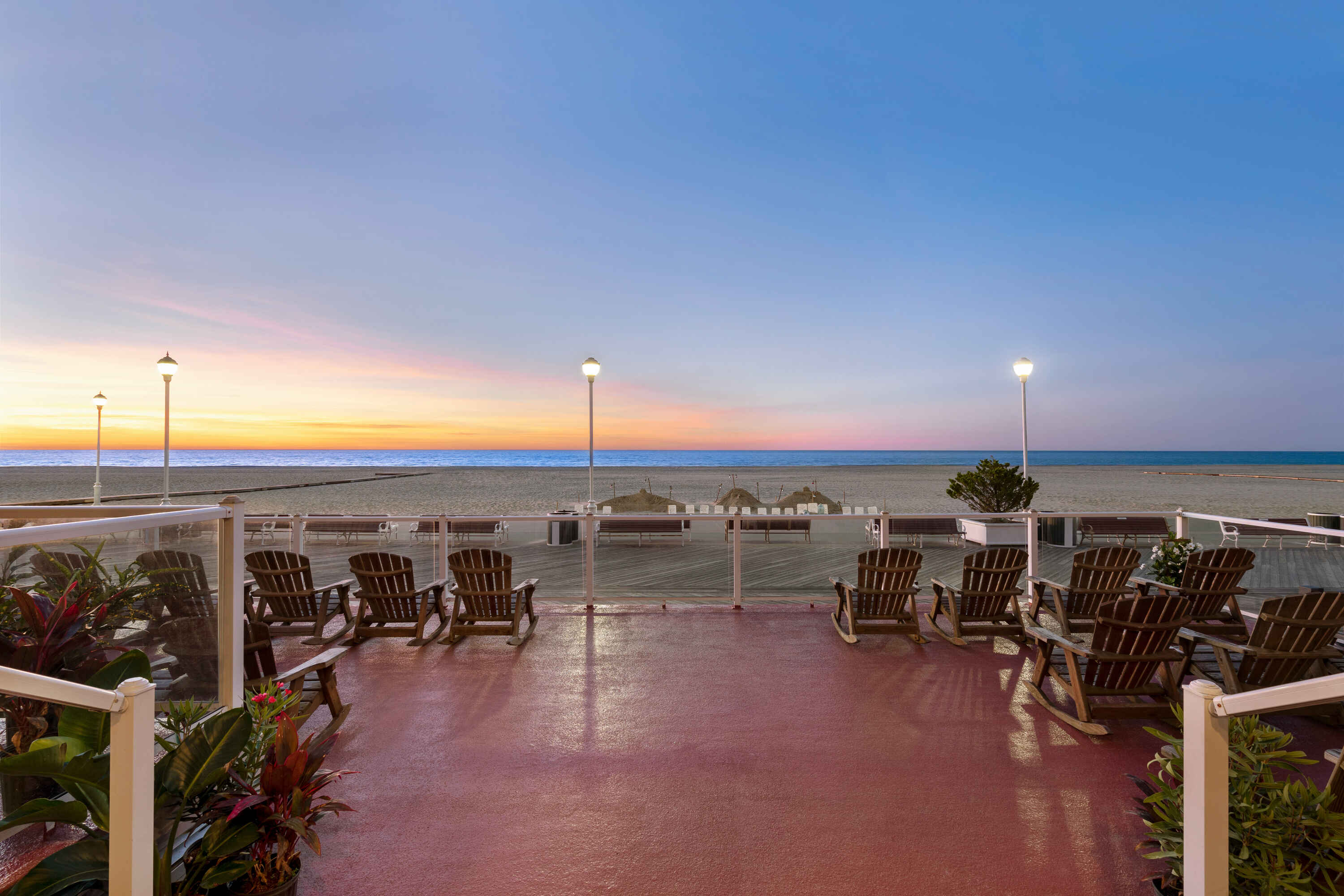 A beachside seating area with rocking chairs and a view of the ocean at sunset.