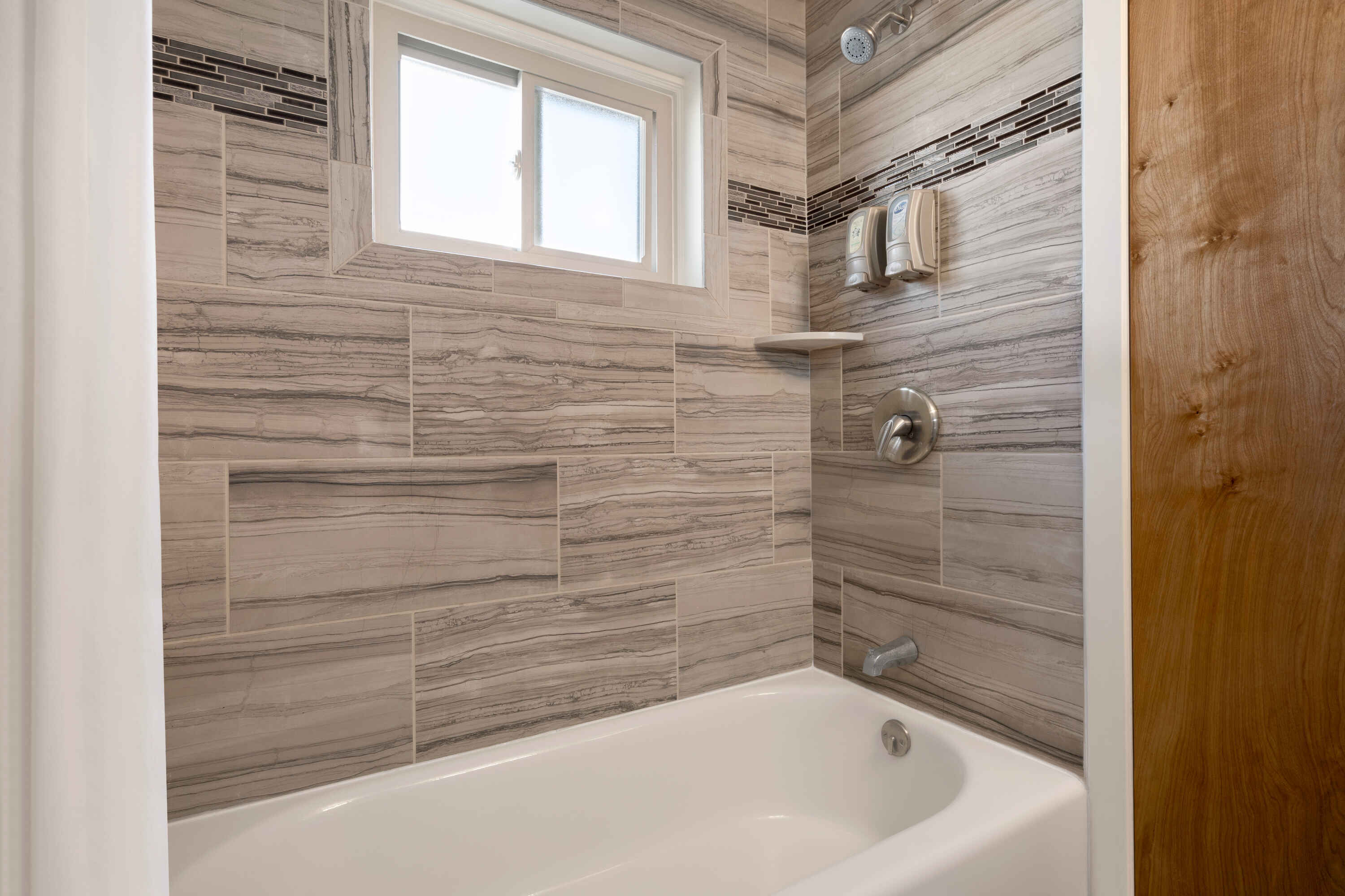 A bathroom with a white bathtub, tiled walls, and a window above the tub.