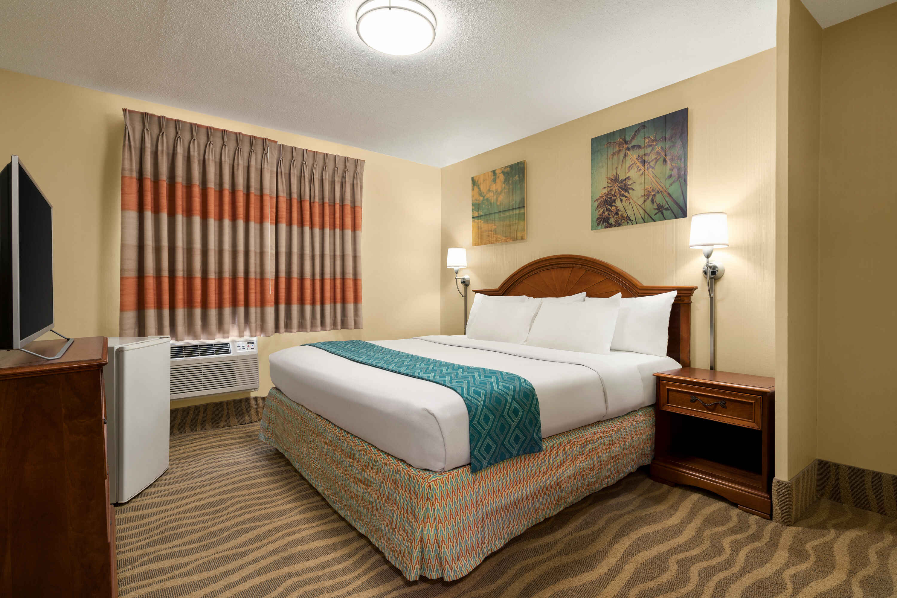 A hotel room with a bed, nightstand, TV, and window