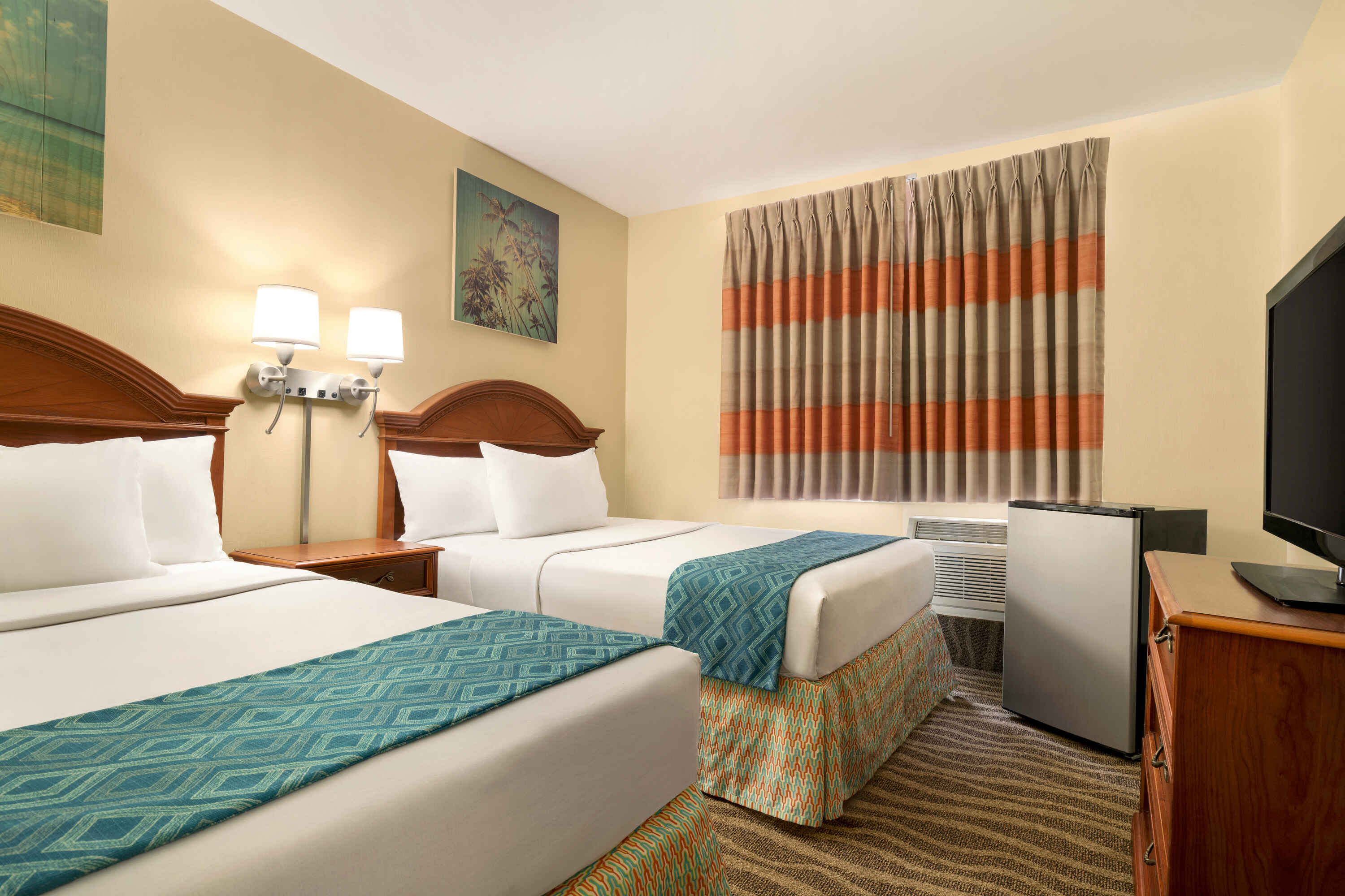 A hotel room with two beds, a TV, a refrigerator, and a window.