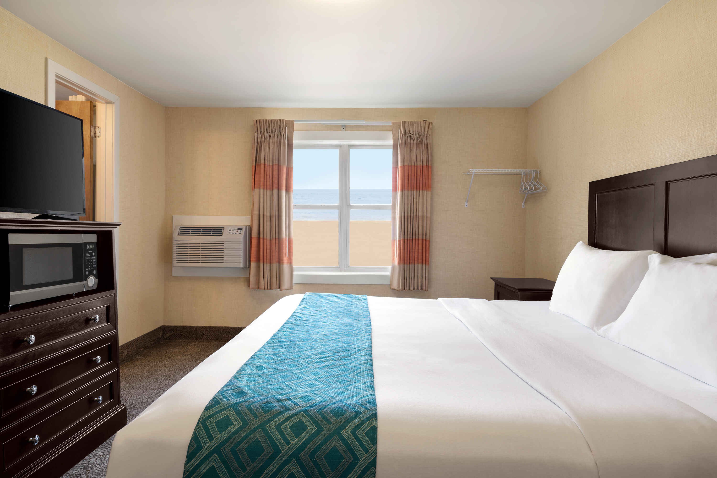 A hotel room with a king-sized bed, flat-screen TV, microwave, and ocean view.