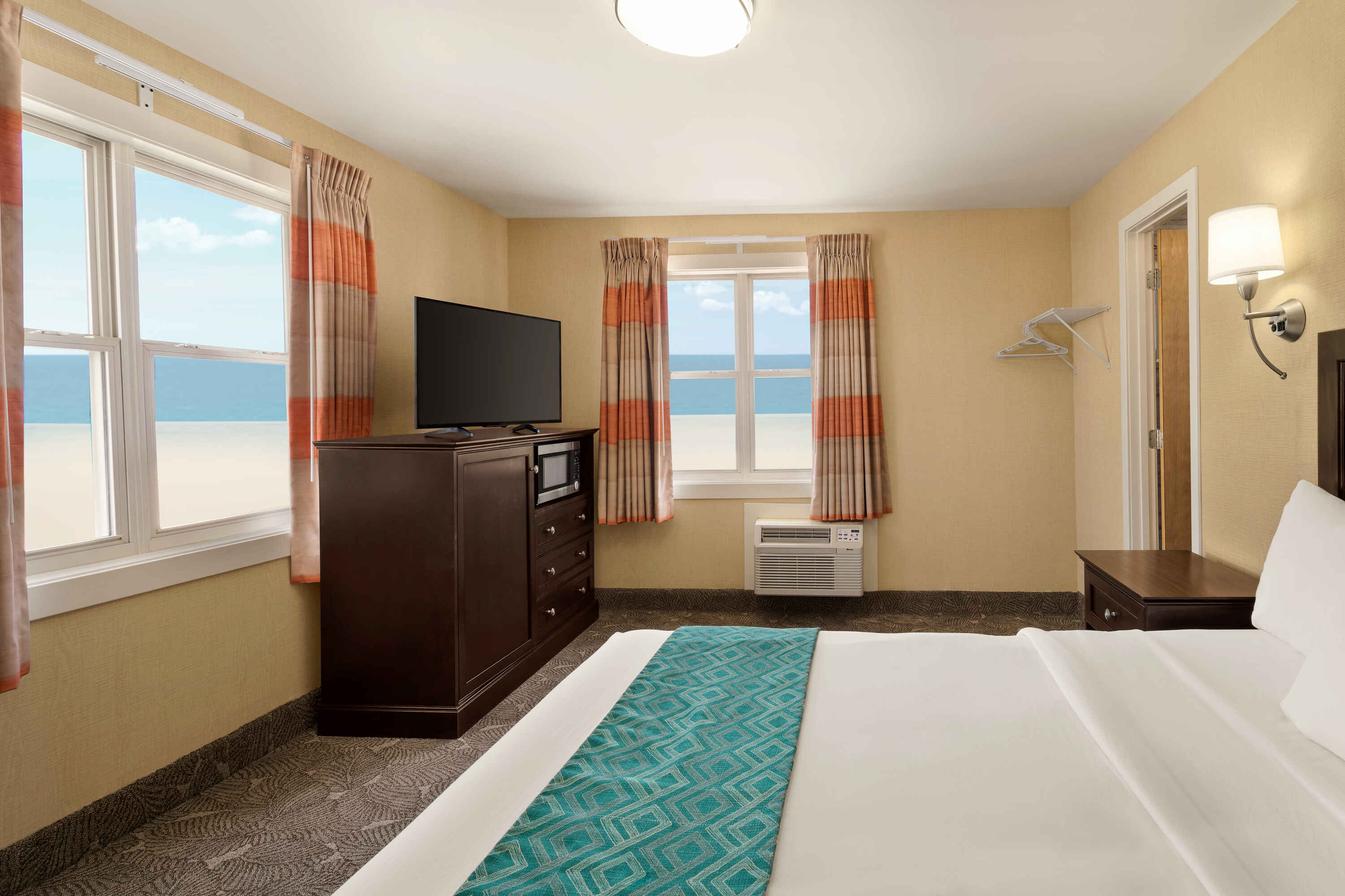 A hotel room with a bed, TV, and window showing the ocean.