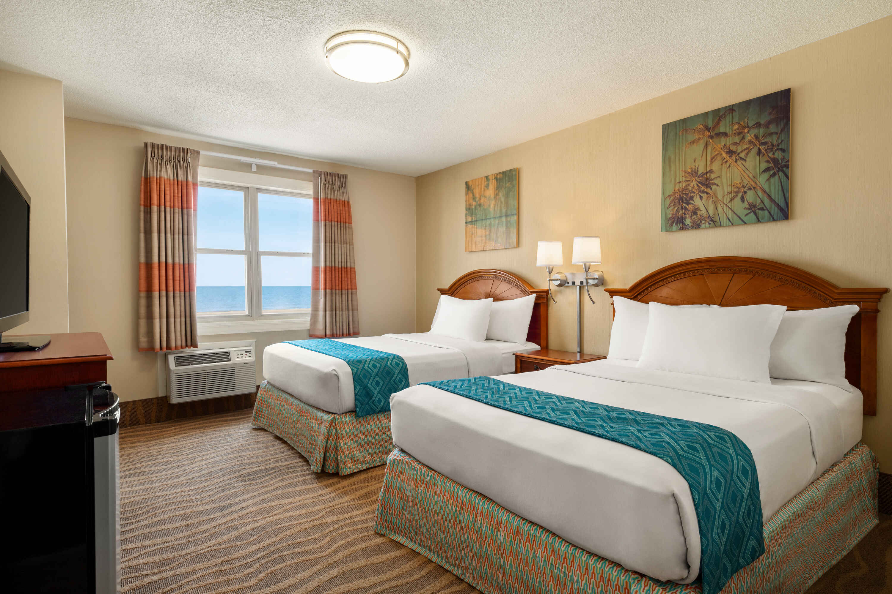 A hotel room with two beds, a window with ocean view, and artwork on the walls.