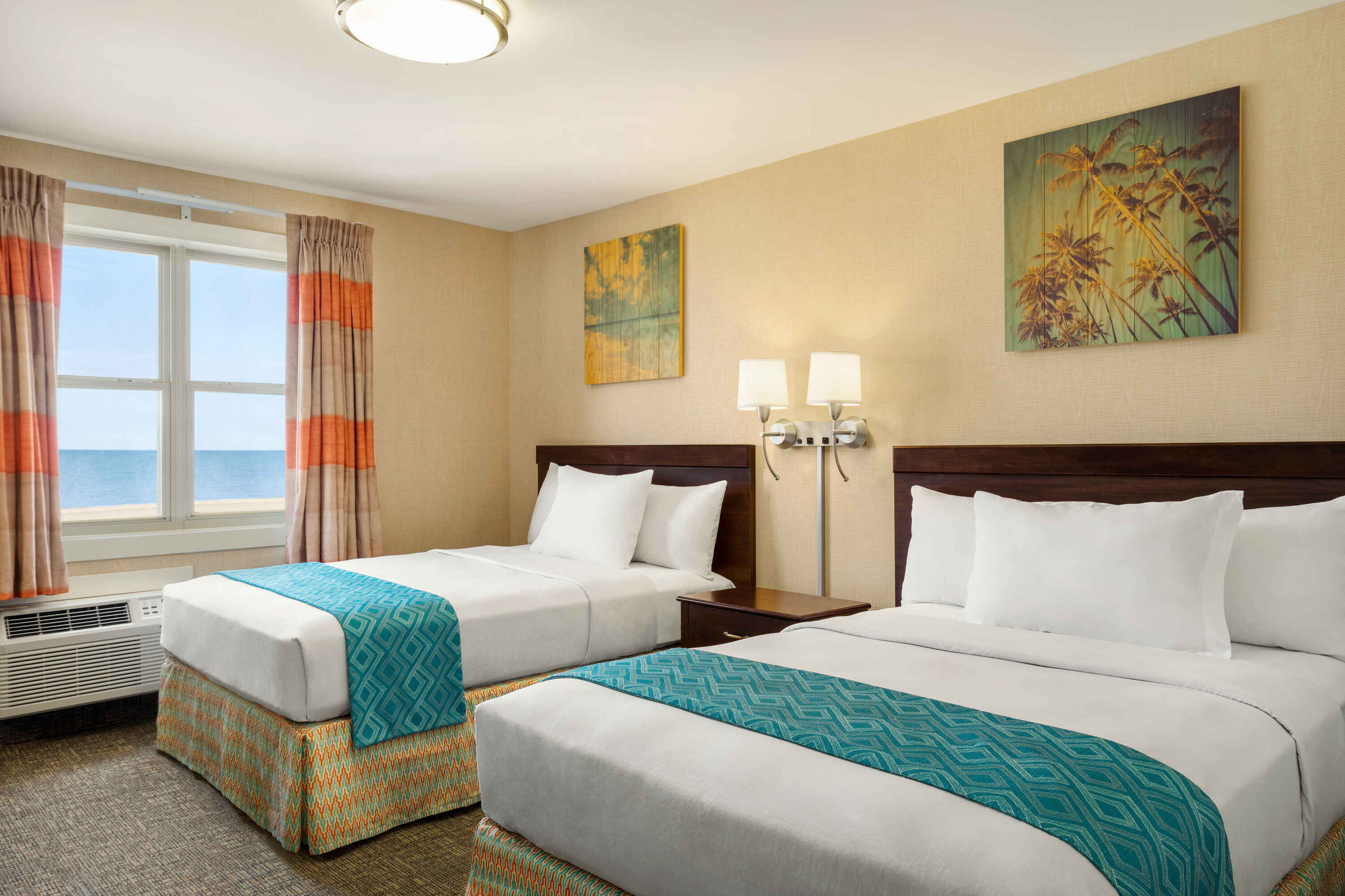 A hotel room with two beds, a window with an ocean view, and artwork on the walls.