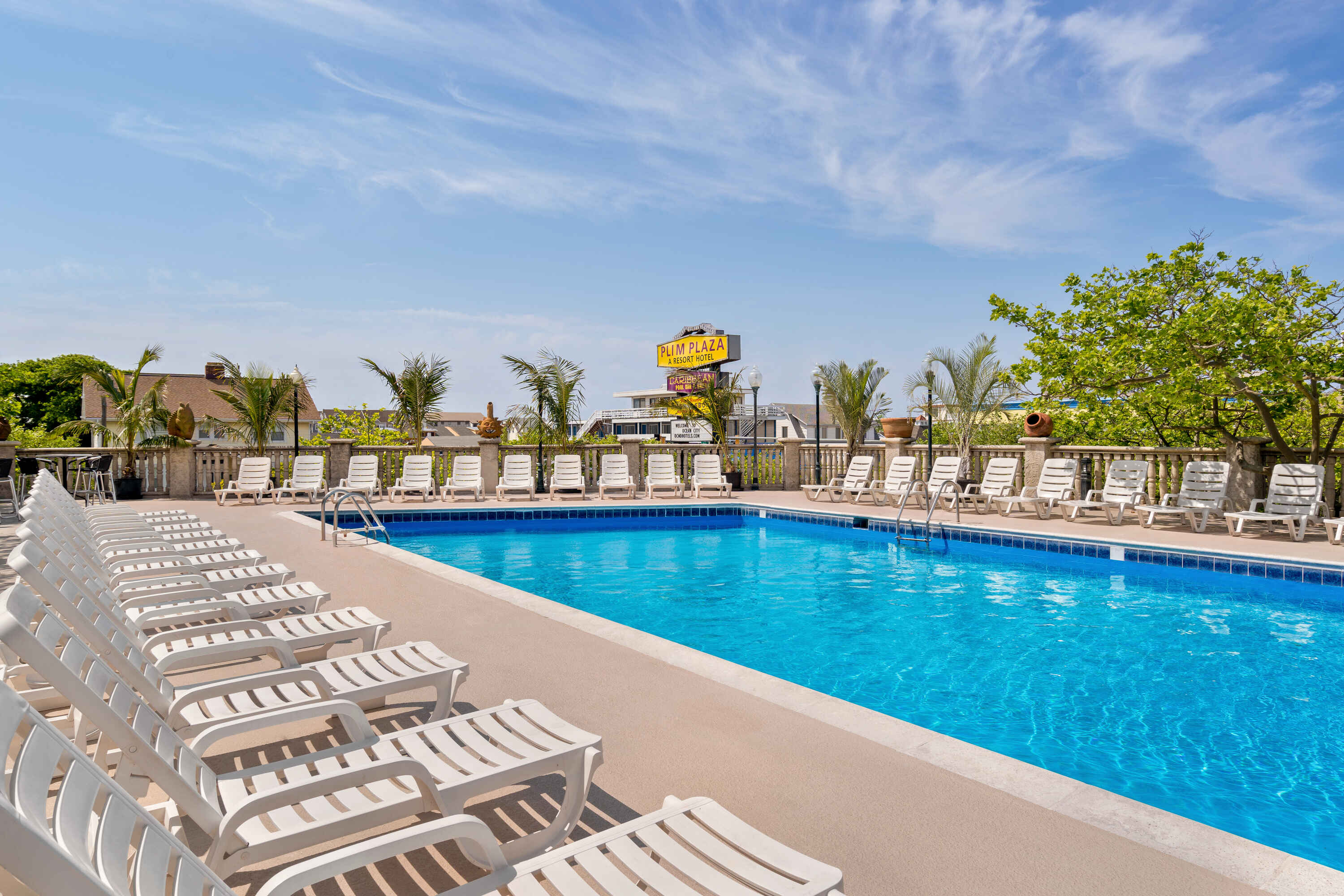 A swimming pool with white lounge chairs and palm trees under a blue sky.