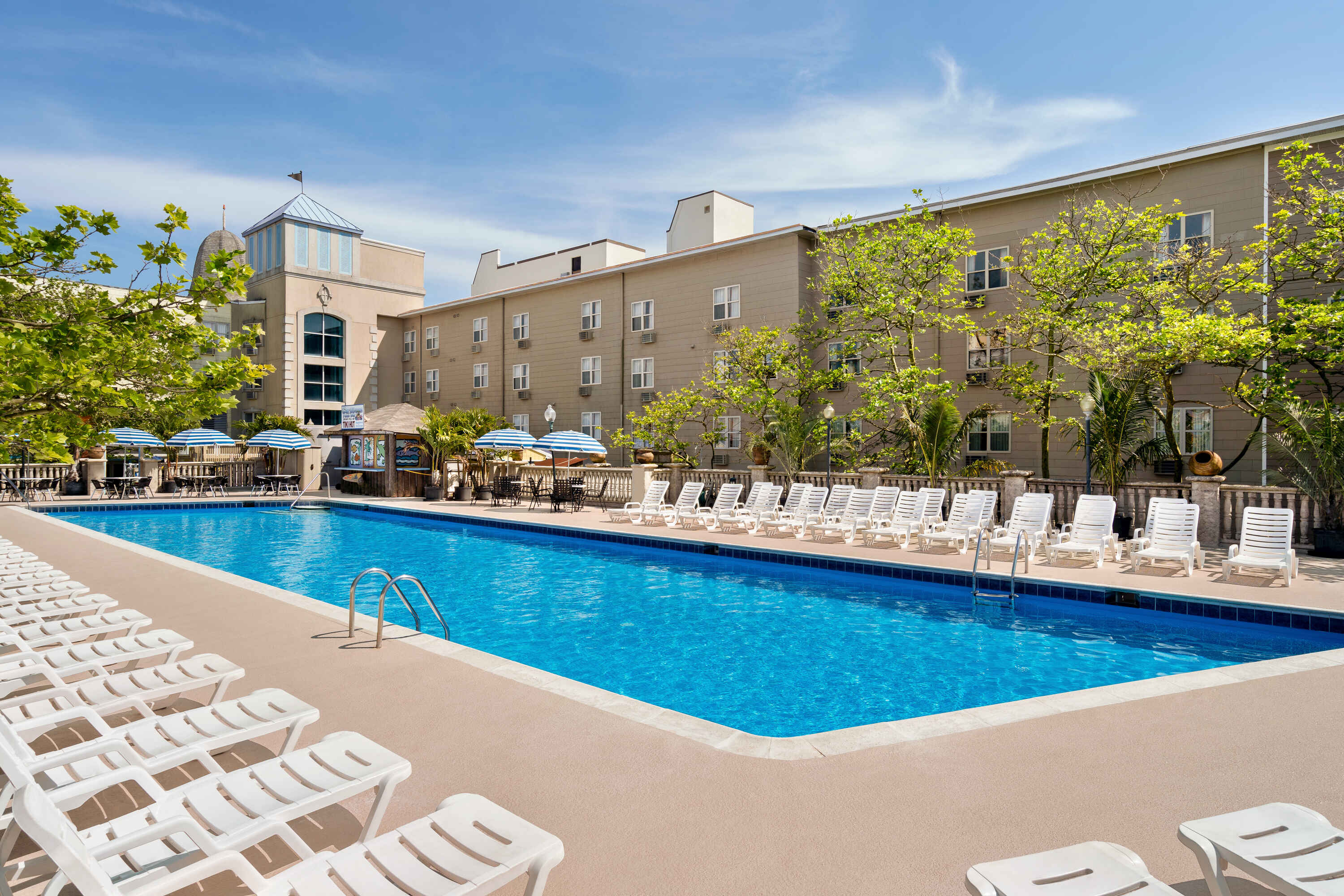 A large swimming pool with lounge chairs and a beige building in the background.