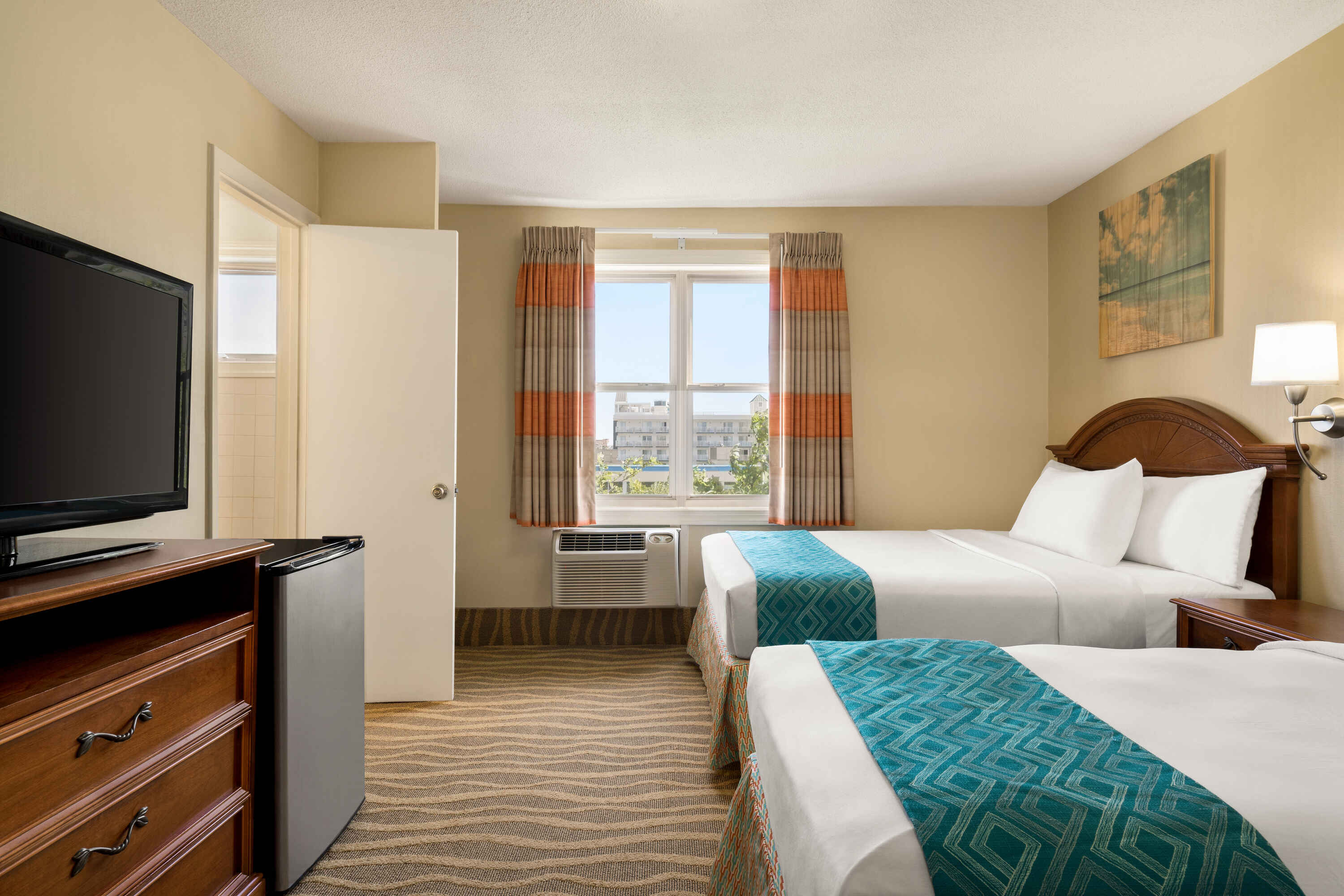 A hotel room with two beds, a TV, a window, and a refrigerator.