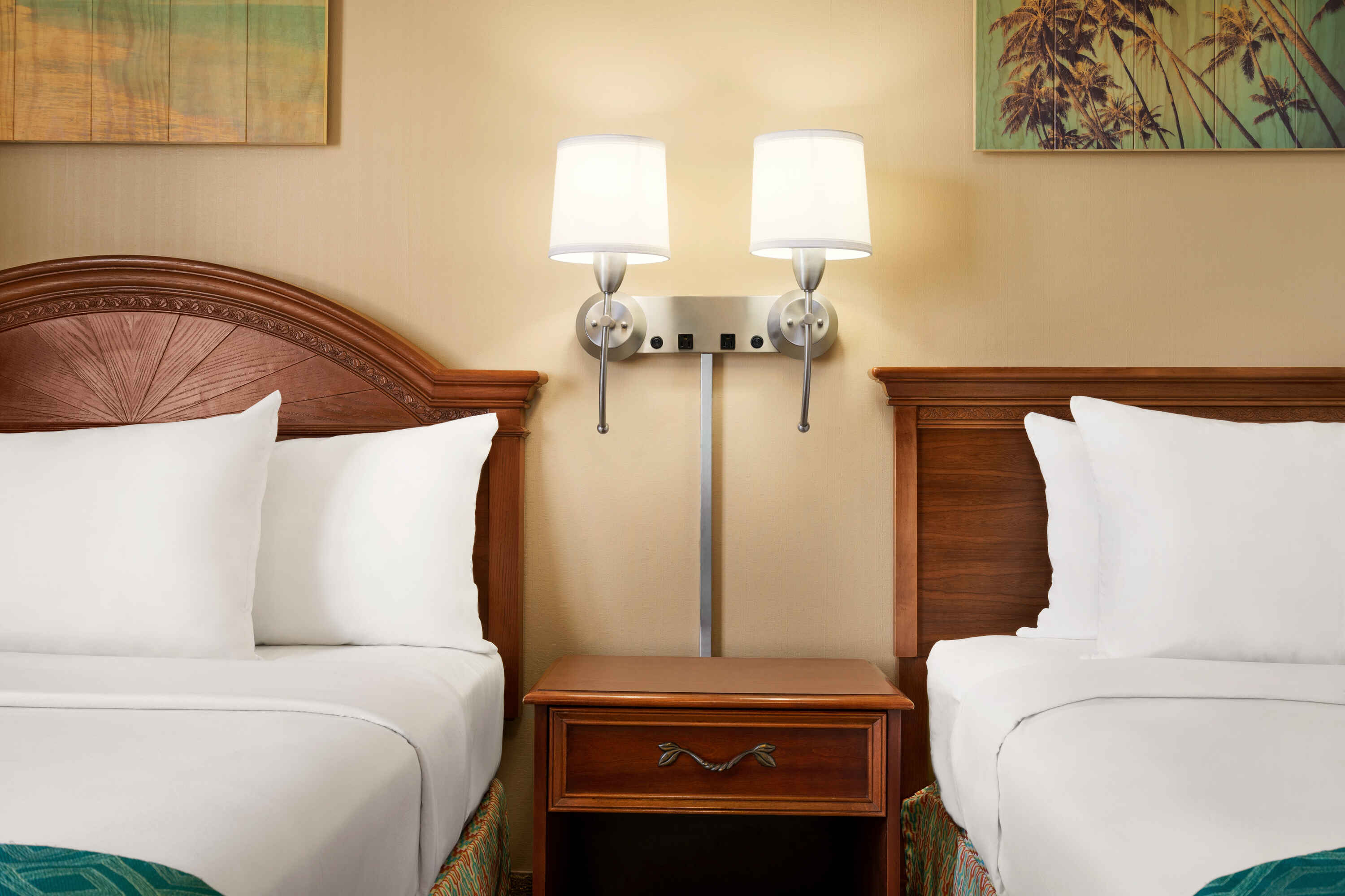 A hotel room with two beds, a nightstand, and a lamp.