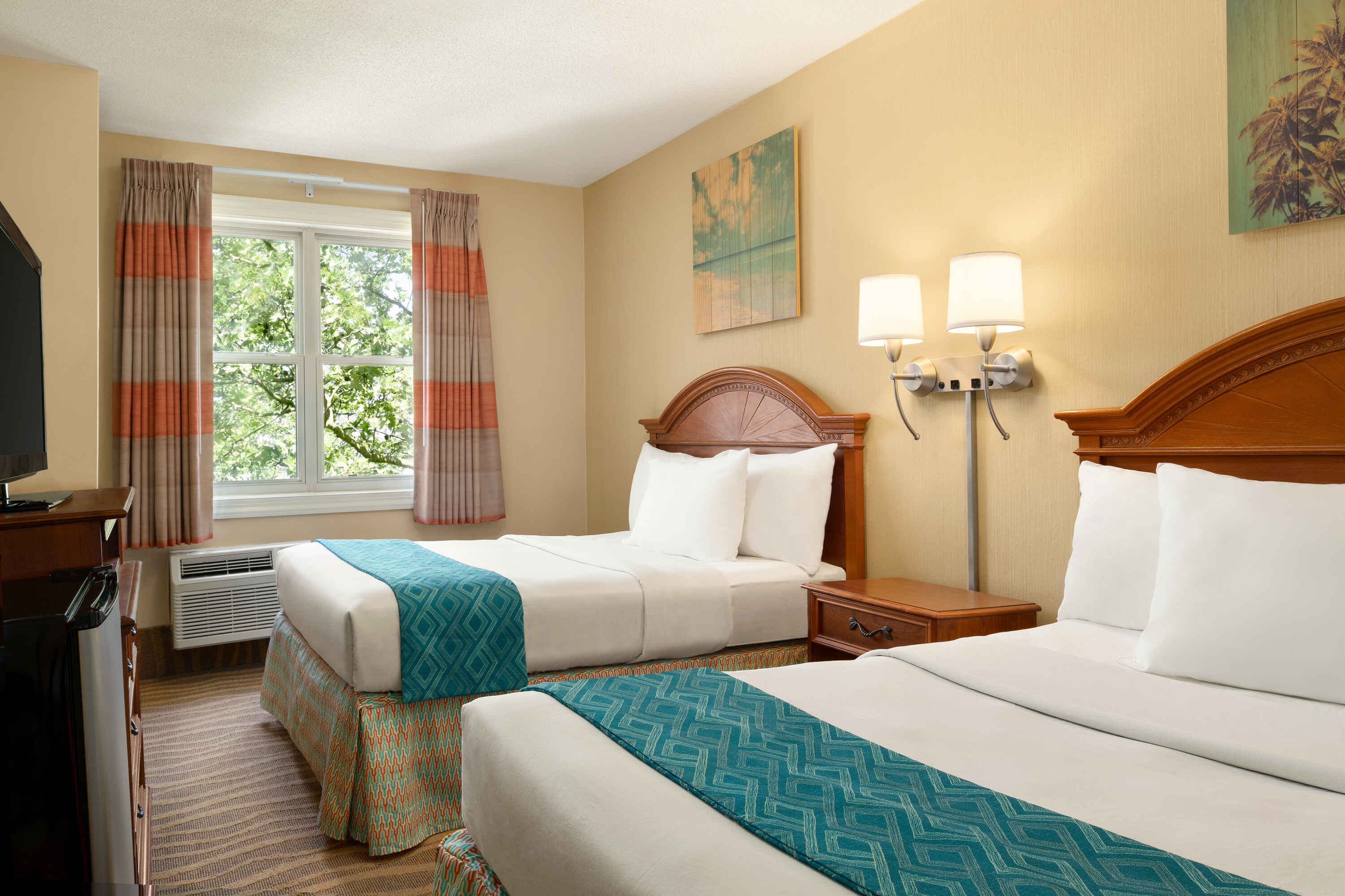 A hotel room with two twin beds, wooden headboards, and white linens, with a window showing a view of trees outside.